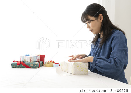 一個女人在客廳的桌子上用包裝紙包裝禮物 84489376