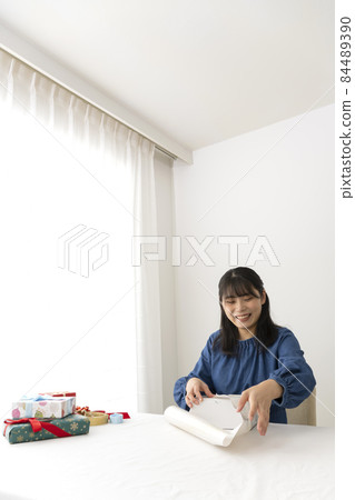 A woman wrapping a gift in wrapping paper at the living room table A woman wrapping a gift in wrapping paper at the living room table 84489390