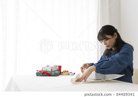 A woman wrapping a gift in wrapping paper at the living room table A woman wrapping a gift in wrapping paper at the living room table 84489391