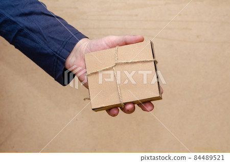 An adult male is holding a brown gift box in his hand. The recta An adult male is holding a brown gift box in his hand. The recta 84489521