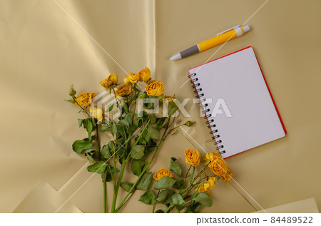 Faded flowers and a blank open notebook with a pen against a cre Faded flowers and a blank open notebook with a pen against a cre 84489522