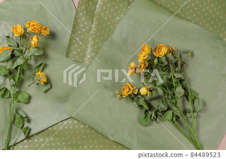 Fading yellow roses on crumpled wrapping paper. Green sheets of Fading yellow roses on crumpled wrapping paper. Green sheets of 84489523