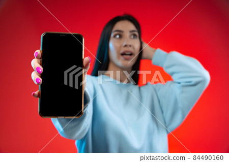 Phone screen. Blurred image of young beautiful girl showing phone isolated over red background Phone screen. Blurred image of young beautiful girl showing phone isolated over red background 84490160