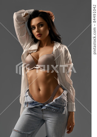 Woman with slim body posing in studio in jeans and shirt Woman with slim body posing in studio in jeans and shirt 84491042