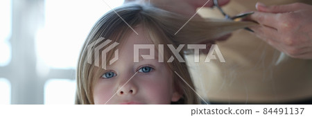 Woman scissors hair of cute blonde little girl closeup 84491137