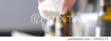 Woman hand pours fine salt into saucepan closeup 84491173