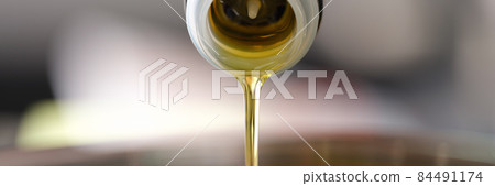 Clear olive oil is poured from dispenser bottle into saucepan closeup 84491174