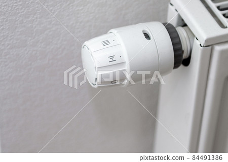 white temperature control knob on white radiator. metal radiator on front of white wall. roman numerals 84491386