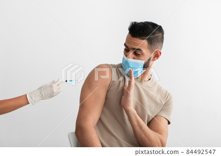 Young Arab guy in disposable mask stopping doctor from making coronavirus vaccine shot, being against covid immunization 84492547