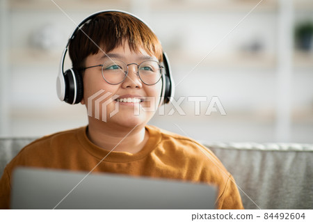 Closeup of cheerful asian kid with wireless headset using laptop 84492604