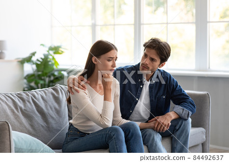 Serious careful young european guy calms upset unhappy lady in living room interior Serious careful young european guy calms upset unhappy lady in living room interior 84492637