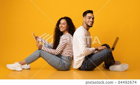 Cheerful arab couple sitting back to back with laptop and digital tablet 84492674