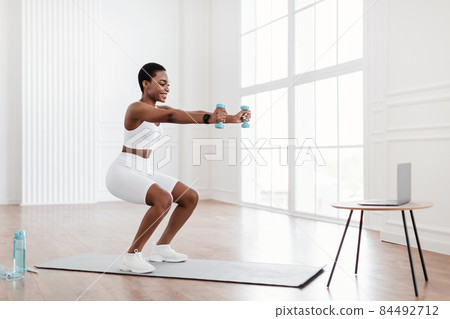 Young black woman exercising with dumbbells in front of laptop 84492712