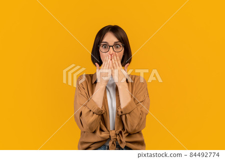 Human emotions and feelings concept. Shocked young woman covering her mouth with hands and looking at camera Human emotions and feelings concept. Shocked young woman covering her mouth with hands and looking at camera 84492774