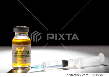 A vial with a medicine for coronavirus on a white table and a syringe. Black background and beam of light, copy space for text, macro 84493635