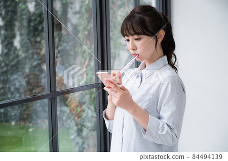 A woman brushing her teeth with a smartphone in one hand A woman brushing her teeth with a smartphone in one hand 84494139