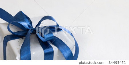 Grey Wrapped Christmas present with a blue ribbon bow on grey close up Grey Wrapped Christmas present with a blue ribbon bow on grey close up 84495451