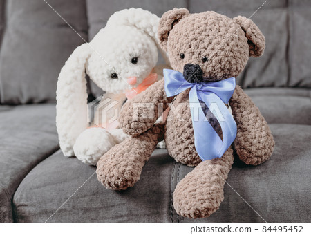 knitted teddy bear and rabbit sitting and talking on a sofa. hand made kids gifts, hobby for meditation and relaxation. knitted teddy bear and rabbit sitting and talking on a sofa. hand made kids gifts, hobby for meditation and relaxation. 84495452
