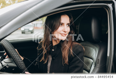 young beautiful brunette woman sitting in a car and driving back. asian woman looking back smiling in a car young beautiful brunette woman sitting in a car and driving back. asian woman looking back smiling in a car 84495454