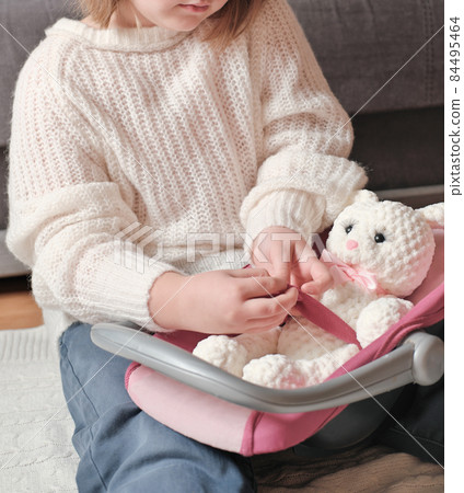 little girl playing with her favorite toy knitted bunny. stuffed hand made toy. girl fastens seat belt on baby car seat. kids safety in a transport. little girl playing with her favorite toy knitted bunny. stuffed hand made toy. girl fastens seat belt on baby car seat. kids safety in a transport. 84495464