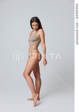 Full-length portrait of young beautiful slim girl in underwear posing isolated over gray studio background. Natural beauty concept. 84495804