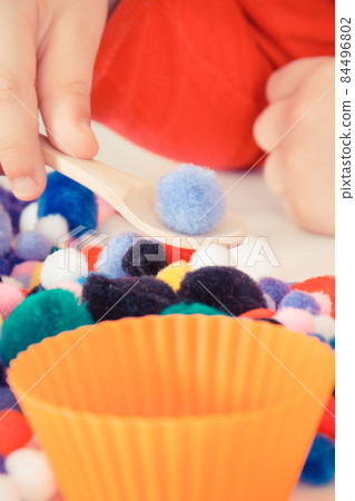 Preschooler playing with small pompoms, wooden spoon and cups. Development of kids motor skills 84496802