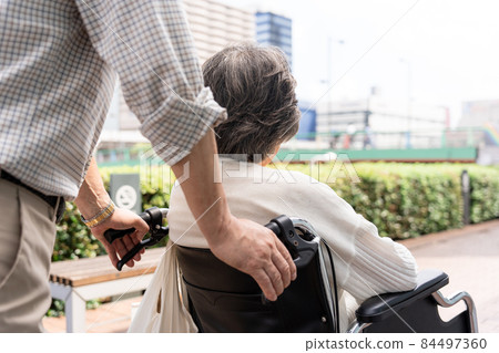 Senior couple wheelchair walk at hand Senior couple wheelchair walk at hand 84497360