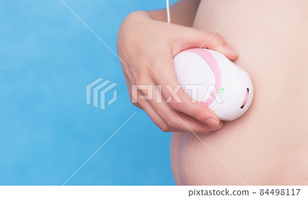 Pregnant girl holds in her hand a fetal doppler near the abdomen and listens to the heartbeat of the child, close-up, stomach 84498117