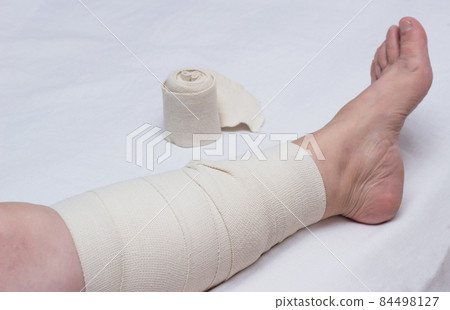 Leg of an elderly woman bandaged with an elastic bandage against varicose veins on the leg, close-up, white background, phlebeurysm 84498127