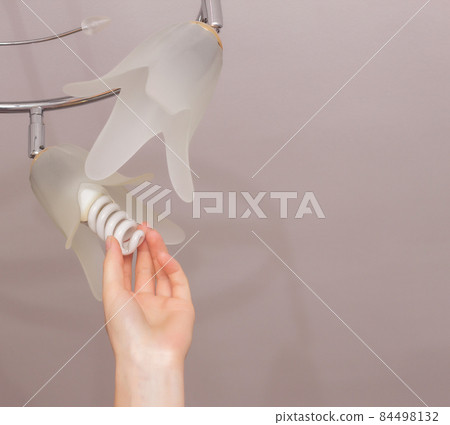 Installing an energy-saving light bulb in the ceiling chandelier, arm, close-up, economical 84498132