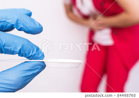 Doctor in a medical glove holding a spoon with medicine in the background a girl holding her stomach, stomach pain, gastritis, close-up Doctor in a medical glove holding a spoon with medicine in the background a girl holding her stomach, stomach pain, gastritis, close-up 84498768