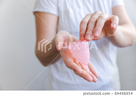 Woman hand holding pink menstrual cup isolated on white background. Woman modern alternative eco gynecological hygiene in menstruation period. Container for blood in girl hand 84498854