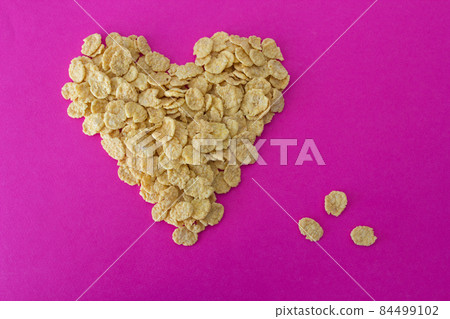 Cornflakes on a pink background in the form of a heart 84499102