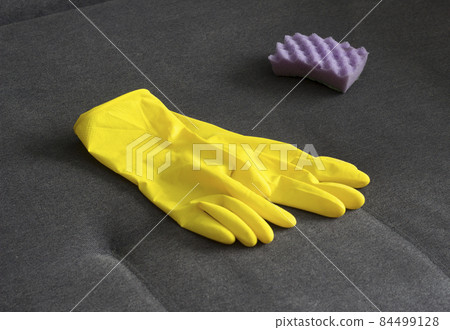 Yellow cleaning gloves and a sponge on the couch, close-up 84499128