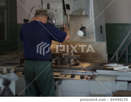 A man specializes a driller drilling holes on a drilling machine in a metal workpiece, a small business, private workshop, bench 84499230