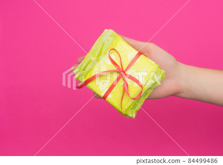 Female hand holding a stack of sanitary pads tied with a red ribbon in her hand, pink background, copy space, critical days 84499486
