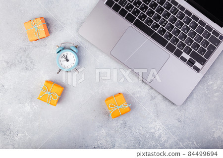 Laptop and orange presents on blue table flat lay. Holiday online shopping concept. Laptop and orange presents on blue table flat lay. Holiday online shopping concept. 84499694