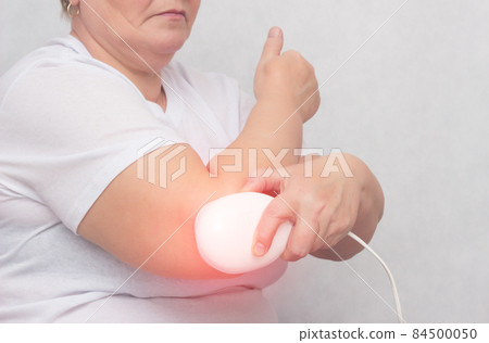 An adult woman treats the elbow joint with a magnetic field, relieves pain and inflammation with a medical magnet, physiotherapy, copy space An adult woman treats the elbow joint with a magnetic field, relieves pain and inflammation with a medical magnet, physiotherapy, copy space 84500050