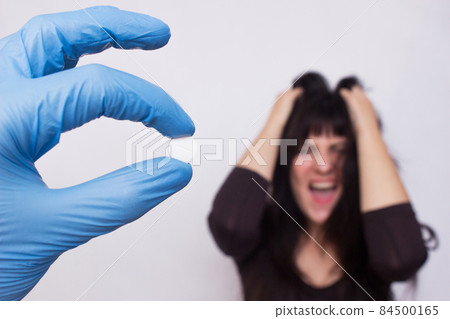 The doctor holds a pill for mental disorders, in the background a girl who has psychosis, emotion, close-up The doctor holds a pill for mental disorders, in the background a girl who has psychosis, emotion, close-up 84500165