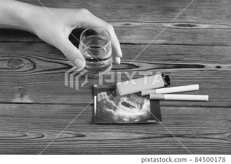 A woman's hand holds a glass of alcohol, next to it is a photograph of the uzi pregnancy and cigarettes, pregnancy and smoking, cigarette 84500178