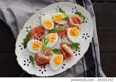 Italian salad. Boiled eggs with smoked ham and arugula on white plate. Dark wooden background 84501142