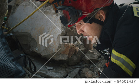 Male rescuer examining rubble and talking 84501437