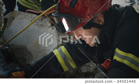 Male rescuer examining rubble and talking 84501448