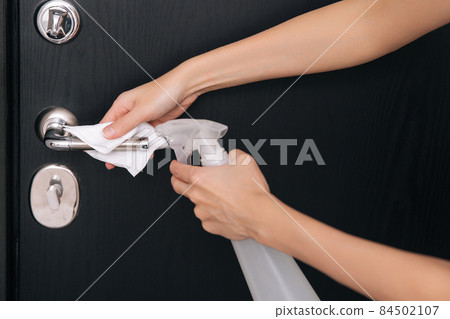 Cleaning black door handles with an antiseptic wet wipe and sanitizer spray. Disinfection in hospital and public spaces against corona virus. Woman hand using towel for cleaning home room door link. 84502107