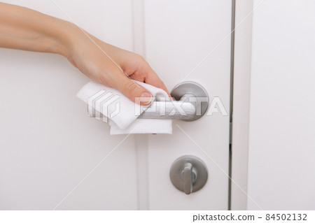 Cleaning door handles with an antiseptic wet wipe and gloves. Sanitize surfaces prevention in hospital and public spaces against corona virus. Woman hand using towel for cleaning home room door link. 84502132