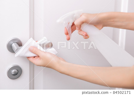 Cleaning white door handles with an antiseptic wet wipe and sanitizer spray. Disinfection in hospital and public spaces against corona virus. Woman hand using towel for cleaning home room door link. 84502171