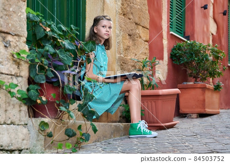 Pre-adolescent schoolgirl with a book sitting on steps of outdoor Pre-adolescent schoolgirl with a book sitting on steps of outdoor 84503752