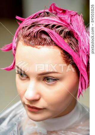The professional hairdresser uses a brush to apply the pink dye to the hair. Hair coloring concept. The professional hairdresser uses a brush to apply the pink dye to the hair. Hair coloring concept. 84503826