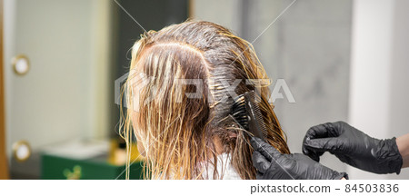 A hairdresser in black gloves is applying brush color to the hair of a customer. Hair coloring in a beauty salon close-up. 84503836