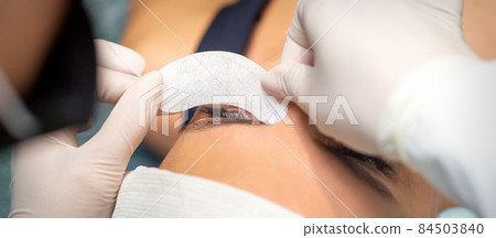The beautician is gluing a patch under her eyes, before the procedure of eyelash extension. Artificial extended eyelashes. The beautician is gluing a patch under her eyes, before the procedure of eyelash extension. Artificial extended eyelashes. 84503840